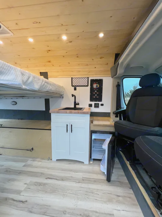 Explore this RV rental's well-designed camper van interior featuring a comfortable bed, compact kitchen, and fridge.. Ram Promaster 1500 2020