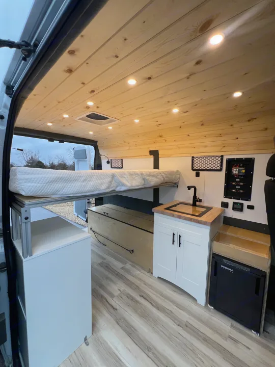 Cozy RV rental interior with raised bed, sink, fridge, and storage. Perfect for adventure.. Ram Promaster 1500 2020