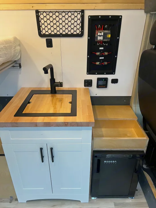 RV rental: a functional kitchenette with sink, wood counter, white cabinets, pull-out storage, Bodega cooler, and electrical panel.. Ram Promaster 1500 2020