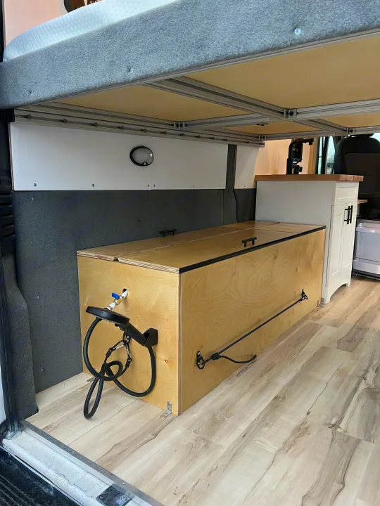 RV rental interior: bed platform, under-bed storage box with external shower, and cabinet in a camper van.. Ram Promaster 1500 2020