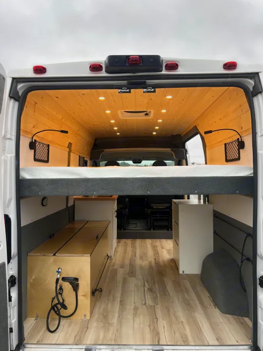 Modern RV rental camper van interior: raised bed, wood ceiling, storage, and shower. Ideal for mobile adventures.. Ram Promaster 1500 2020