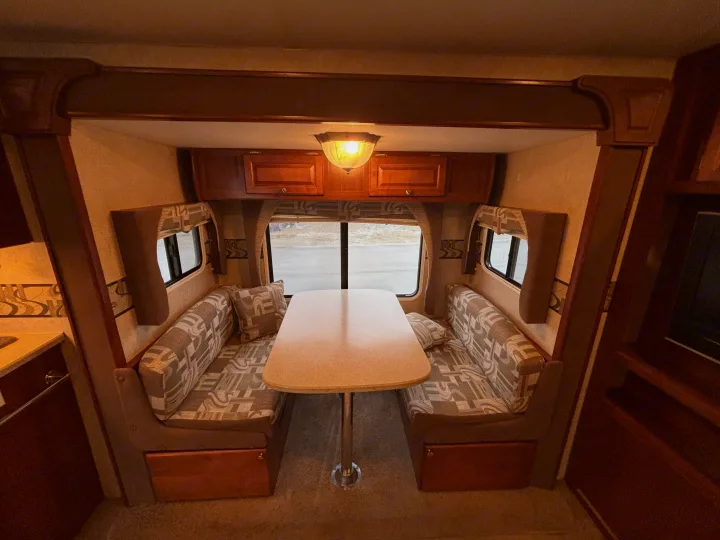 Spacious RV rental dinette area with comfortable bench seating, table, and storage cabinets, ideal for mobile living.. Fleetwood 230RKS 2009
