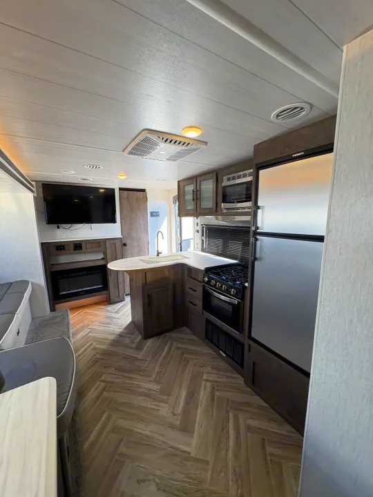 This rv rental features a modern kitchen, living space with TV, fireplace, and comfy dinette, all on herringbone flooring.. Forest River Wildwood X-Lite 2022