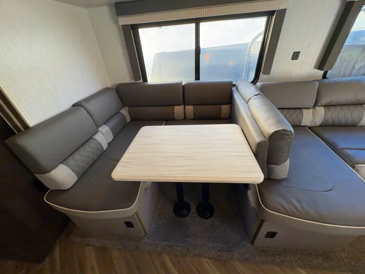 Spacious grey U-shaped dinette with white table in this RV rental's interior, offering ample seating and a modern look.. Forest River Wildwood X-Lite 2022