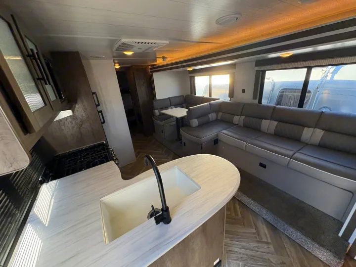 Step into this bright RV rental interior: a modern kitchen with sink and stove, plus a spacious U-shaped dinette seating area.. Forest River Wildwood X-Lite 2022
