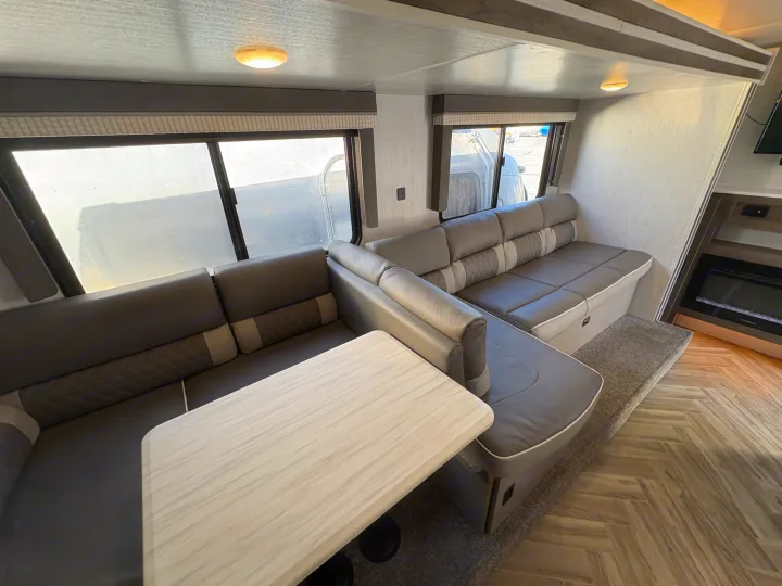 U-shaped dinette seating in a modern RV rental, with gray cushions, a light table, wood-look floor, and windows.. Forest River Wildwood X-Lite 2022