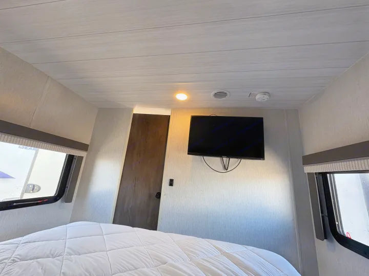 RV rental bedroom with a comfortable bed, wall-mounted TV, and modern textured walls and ceiling.. Forest River Wildwood X-Lite 2022
