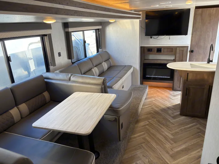 Spacious RV rental interior with a U-shaped dinette, TV, fireplace, and a kitchen area featuring a sink.. Forest River Wildwood X-Lite 2022