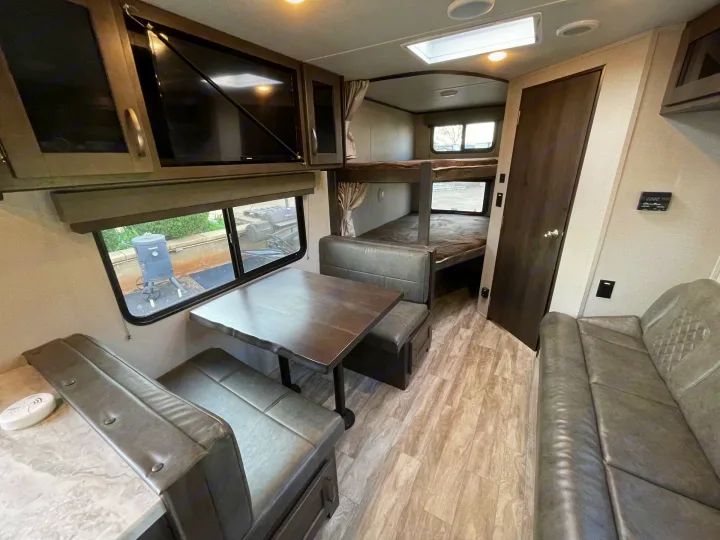 RV rental interior: modern gray dinette, bunk beds, TV, and sofa. Light wood-look floor completes the space.. Grand Design Transcend Xplor 2023