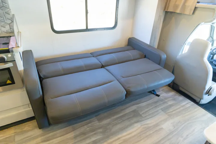 RV rental: Gray sofa bed extended, with kitchen, window, and front cabin seats.. Gulf Stream Conquest 2024