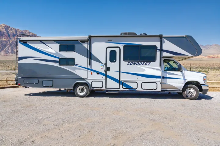 A white and grey Conquest RV rental parked in a desert landscape with mountains under a clear sky. Perfect for outdoor adventures.. Gulf Stream Conquest 2024
