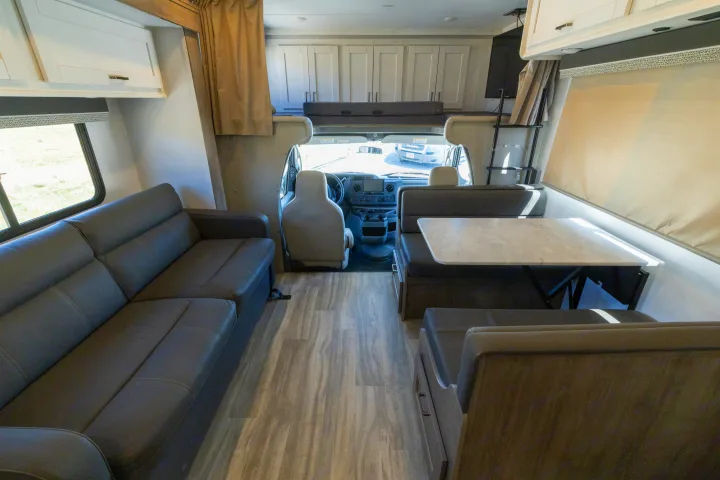 Inside a modern RV rental, featuring a sofa, dinette with table, and overhead sleeping area. Clean and ready for adventure.. Gulf Stream Conquest 2024