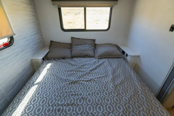 Cozy RV rental bedroom with geometric bedding, natural light, and side shelves. Perfect for a comfortable stay.. Gulf Stream Conquest 2024