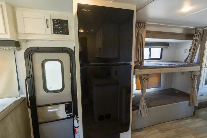 Inside this RV rental: sleek black refrigerator, functional control panel, and cozy bunk beds with privacy curtains.. Gulf Stream Conquest 2024