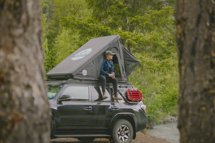 Enjoy nature with this unique RV rental! Person sits on SUV with rooftop tent by a scenic river.. Toyota 4Runner 2025