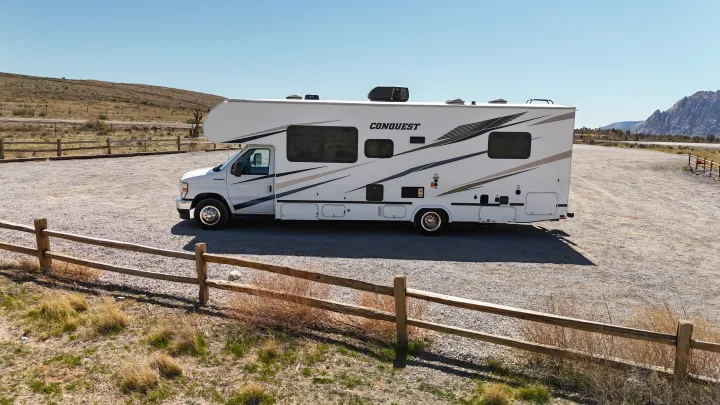 A white Conquest Class C RV rental parked on a sunny gravel lot in a desert landscape, ready for adventure.. Gulf Stream Conquest 2024