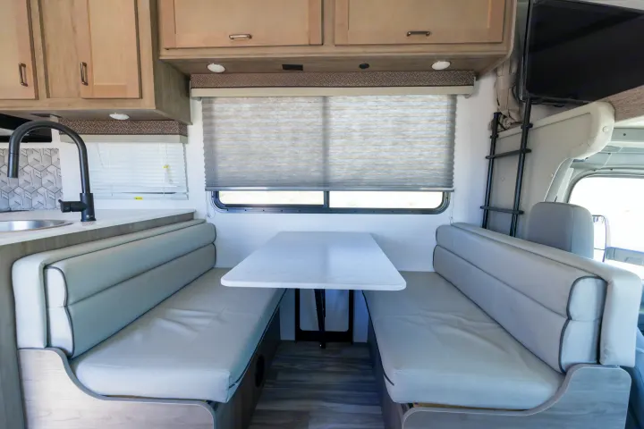 Bright RV rental interior features a cozy dinette, modern kitchen with sink, and ladder for upper bunk access.. Gulf Stream Conquest 2024
