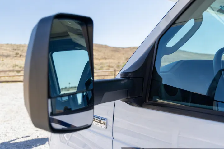 Side view of a white RV rental, showing its large mirror and a Ford F-350 Super Duty emblem in a desert setting.. Gulf Stream Conquest 2024