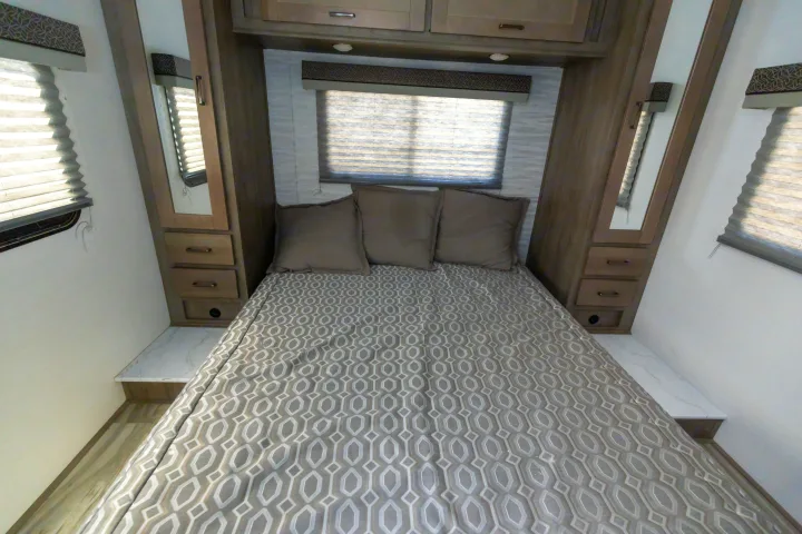 Cozy RV rental bedroom featuring a patterned bed, mirrored side storage, built-in drawers, and windows with blinds for comfort.. Gulf Stream Conquest 2024