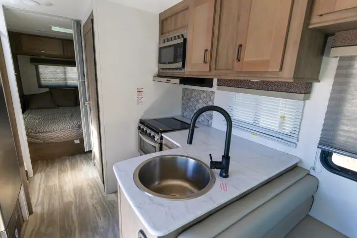 Modern RV rental interior featuring a compact kitchen, dining area, and a view into the bedroom.. Gulf Stream Conquest 2024