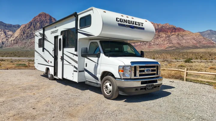 White Conquest RV rental parked in a gravel lot with Red Rock Canyon mountains in the background on a sunny day.. Gulf Stream Conquest 2024