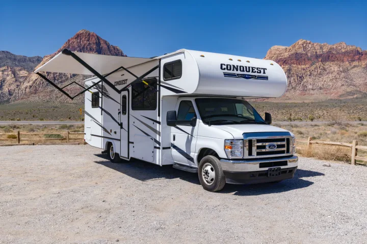 A white Conquest Gulf Stream RV rental with awning extended, parked on gravel in a scenic desert mountain landscape.. Gulf Stream Conquest 2024