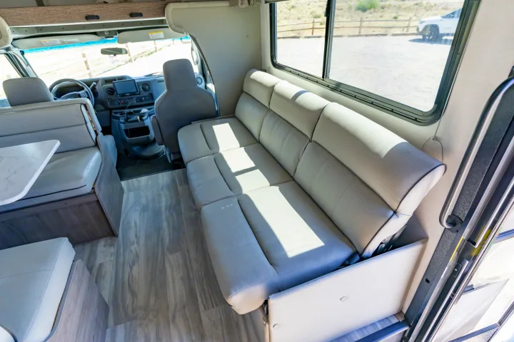Interior of an RV rental, showing the front cockpit, dinette, and sofa lounge area with large windows.. Gulf Stream Conquest 2024