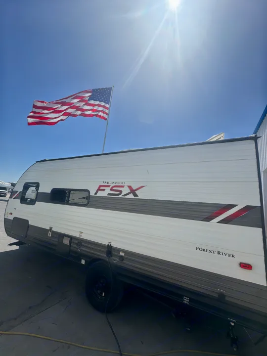 Bright sun illuminates this Wildwood FSX travel trailer RV rental, with an American flag flying proudly in the blue sky.. Forest River Wildwood FSX 2021