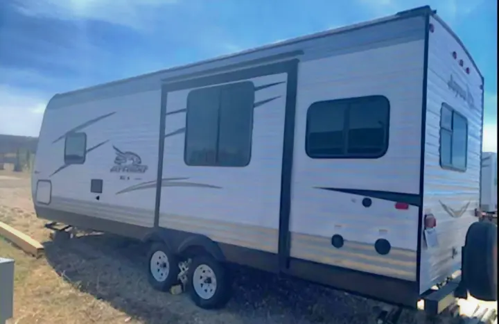 White Jayco travel trailer for RV rental, featuring a large slide-out and windows, parked outdoors.. Jayco Jay Flight SLX 2016