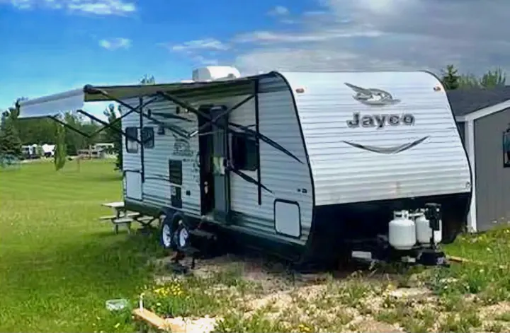 White Jayco travel trailer rv rental with extended awning, parked on a grassy lot under blue skies. Ideal for camping.. Jayco Jay Flight SLX 2016