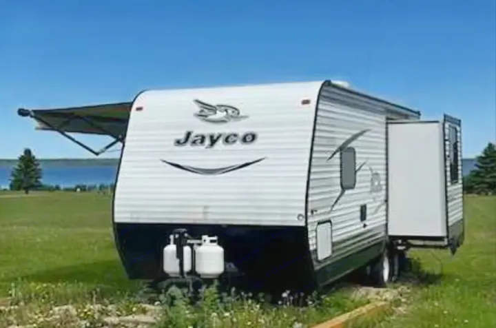 Jayco travel trailer RV rental: Parked by a serene lake, featuring an extended awning & slide-out for spacious camping.. Jayco Jay Flight SLX 2016