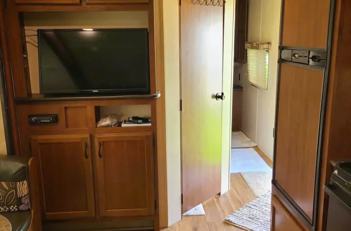 This RV rental offers a well-equipped living area, showcasing a TV, stereo, and storage cabinets, adjacent to the refrigerator and a hallway.. Jayco Jay Flight SLX 2016
