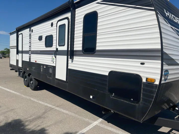 Side view of a large white and black travel trailer, ideal for an rv rental, parked on asphalt under clear skies.. Keystone RV Hideout 2022