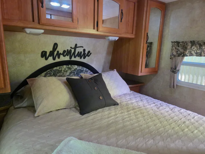 Inside an RV rental: a cozy bedroom featuring a quilted bed, "adventure" wall art, and wooden overhead cabinets.. Keystone RV Sprinter 250RBS 2008