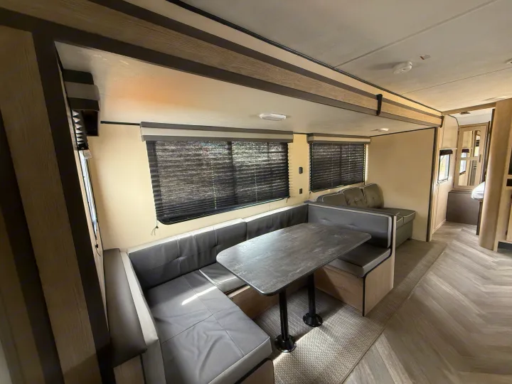 Modern RV rental interior: a spacious dinette with U-shaped seating, a table, and an adjacent lounge area.. Heartland RVs Prowler 2021