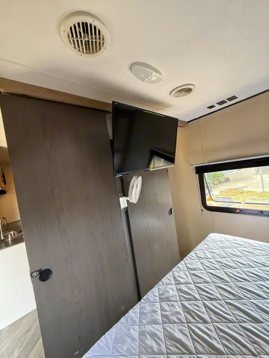 Cozy rv rental bedroom features a bed, TV, fan, and sliding doors, offering comfort for your journey.. Heartland RVs Prowler 2021