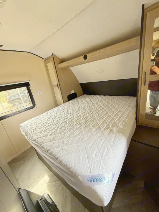 Interior of an RV rental bedroom featuring a clean, quilted bed, overhead storage, and a window with an outdoor view.. Heartland RVs Prowler 2021