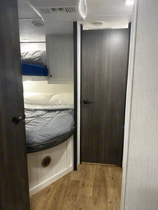 RV rental bunk bed sleeping area. Features two bunks, ceiling AC, and a dark wood door, showcasing compact mobile living.. 5sfeb3729me459252 31DB 2021