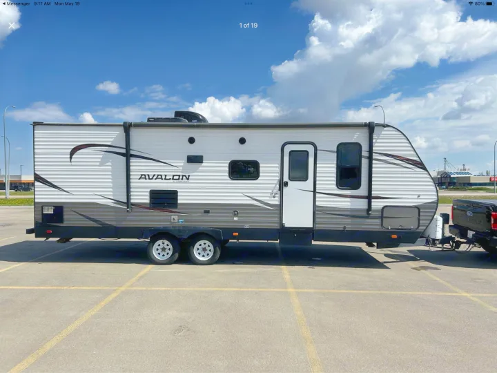 An Avalon by Starcraft travel trailer, ideal for rv rental, is hitched to a truck. The white and grey RV is parked in a sunny lot.. Starcraft Avalon 2018