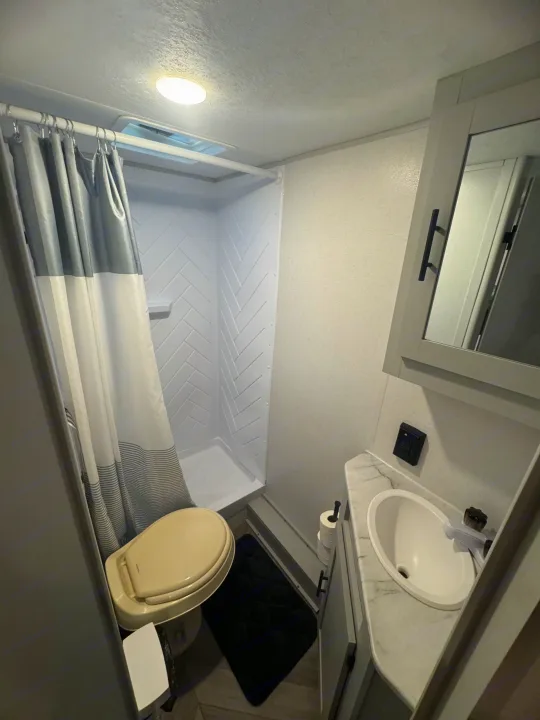 Step into this compact RV rental bathroom, equipped with a shower, toilet, and sink vanity with mirror.. Forest River Wildwood FSX 2021