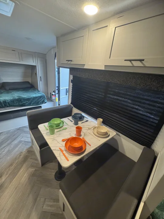RV rental interior: dining area with colorful place settings, a cozy bed, and overhead storage.. Forest River Wildwood FSX 2021