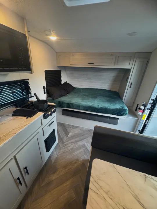 Inside a cozy RV rental: kitchen with stove & microwave, and bed area. Herringbone floor adds style.. Forest River Wildwood FSX 2021
