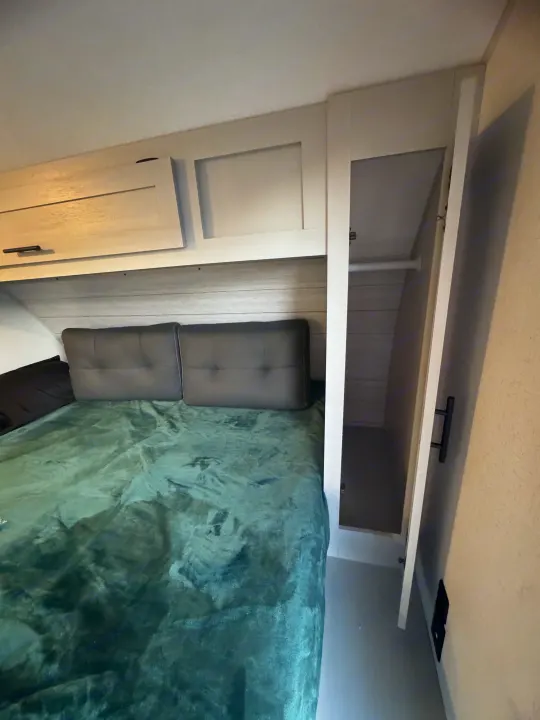 RV rental bedroom featuring a comfy bed, overhead storage, and an open closet with a hanging rod.. Forest River Wildwood FSX 2021