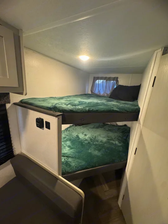Inside an RV rental: two compact bunk beds with soft green blankets. Perfect for family adventures.. Forest River Wildwood FSX 2021