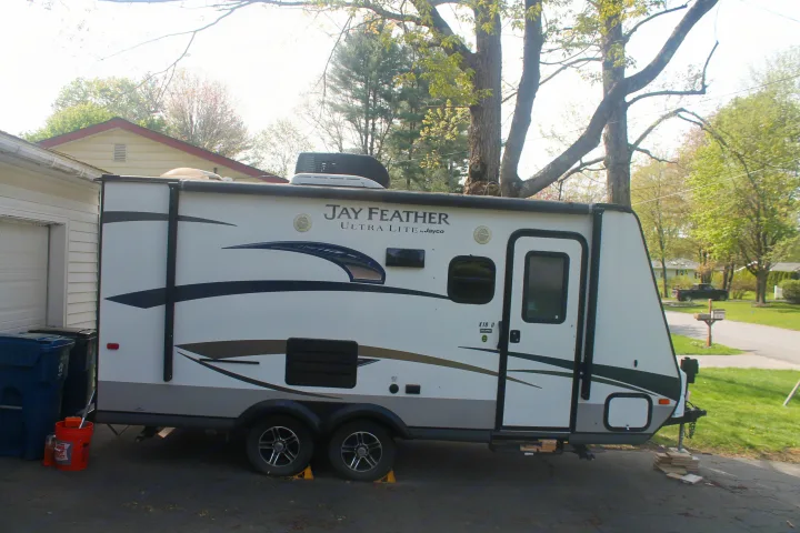 A white Jayco Jay Feather Ultra Lite rv rental travel trailer, with black and gray graphics, parked in a driveway.. Jayco Jay Feather Ultra Lite 2015