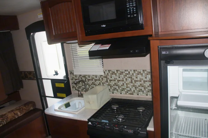 Inside an RV rental, showing the kitchen area with a microwave, stove, sink, refrigerator, and cabinets.. Jayco Jay Feather Ultra Lite 2015