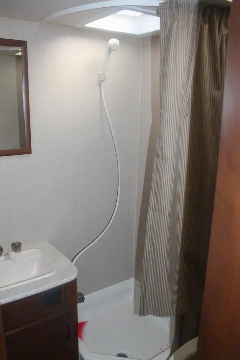 A compact RV rental bathroom featuring a shower with a handheld head, striped curtain, and sink vanity with mirror.. Jayco Jay Feather Ultra Lite 2015