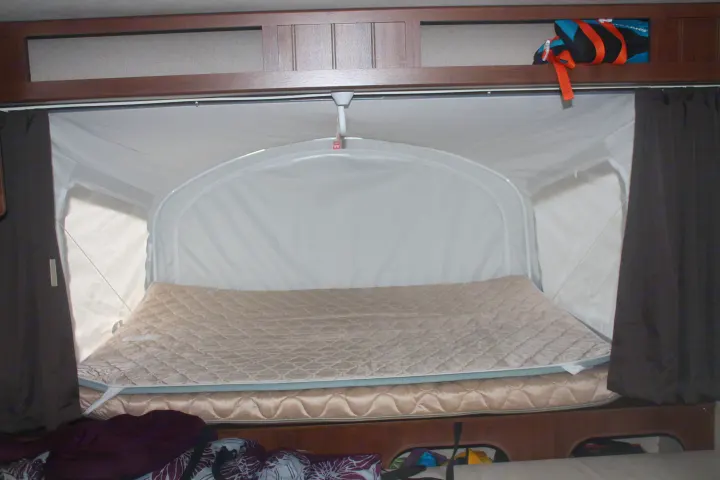 RV rental interior: cozy pop-up bed with quilted mattress, curtains, and overhead storage, perfect for camping comfort.. Jayco Jay Feather Ultra Lite 2015