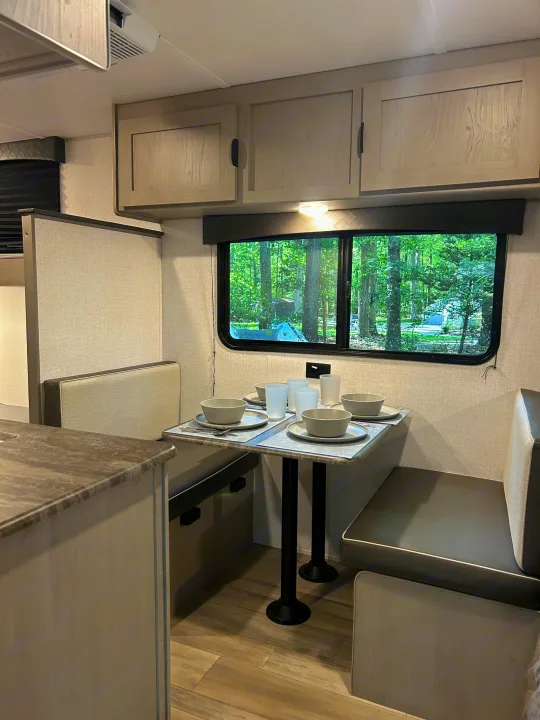 Dine in comfort in this RV rental! View of the modern dinette area, set with dishes, next to a counter and window with trees.. Clipper 17CBHCADET 2024