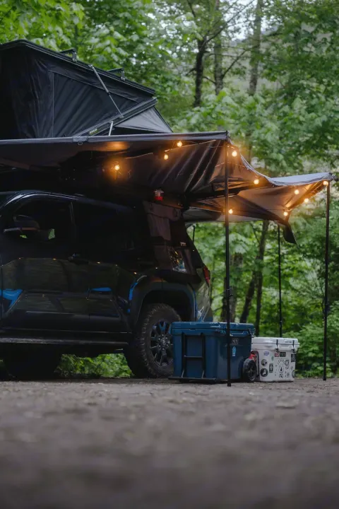 A truck with rooftop tent and illuminated awning creates a cozy outdoor camp. Consider this an RV rental for adventure.. Toyota 4Runner 2025